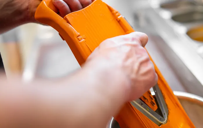 Utilisation d'une mandoline pour découper finement les légumes de garniture d'une pizza